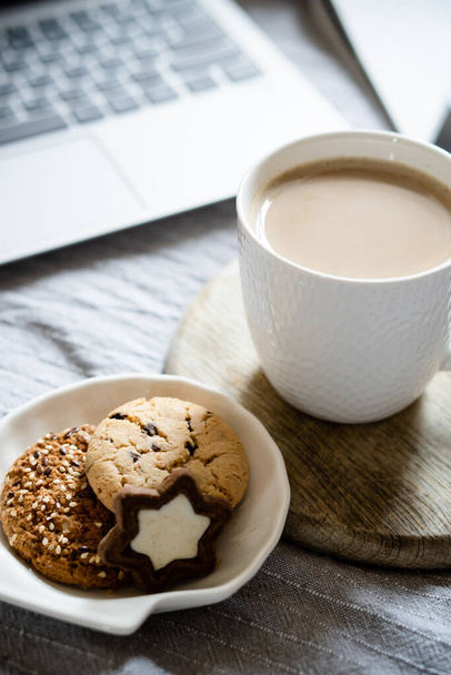 Echter Arbeitsplatz zu Hause, Laptop mit Tasse Kaffee und Keksen auf dem Bett mit kuscheliger Decke - Foto, Bild