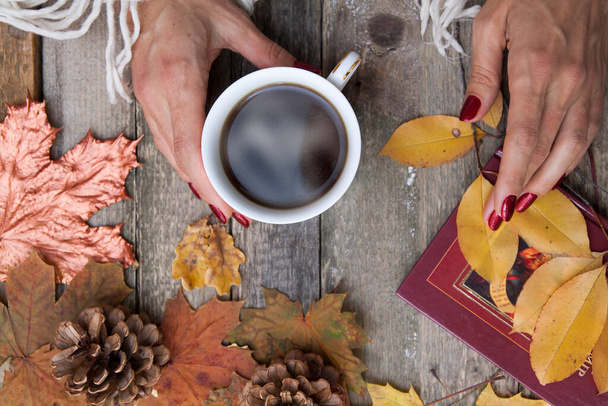 Pohled shora šálek kávy v ženských rukou na dřevěném stole pozadí s podzimními listy, kornouty - Fotografie, Obrázek
