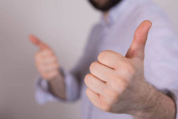 A closeup of a person doing the thumbs-up gesture under the lights against a blurry background - Foto, imagen