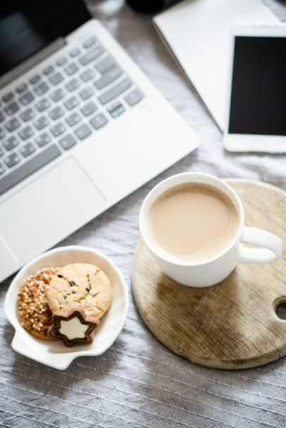 Real home workplace, laptop with cup of coffee with cookies on bed with cozy blanket - Photo, Image