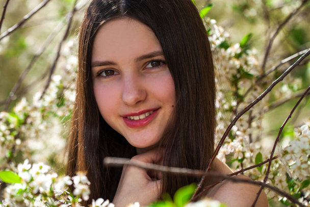 Pretty teen girl are posing in garden near blossom cherry tree with white flowers. Spring time  - Φωτογραφία, εικόνα