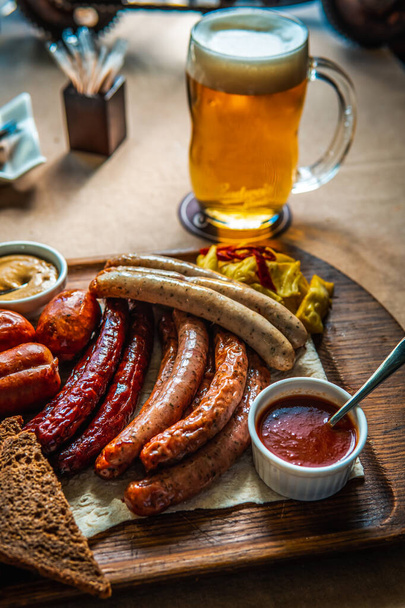 Hunting sausages on a wooden board on the table. Ketchup and mustard and brown bread next to the sausages. Beer snack. - Foto, imagen