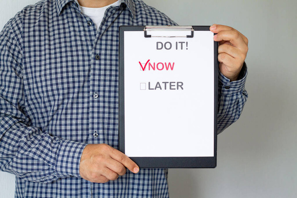 A halogatás és az üzleti koncepció elleni küzdelem. Férfi kezében papír poszter szöveggel "Most vagy később" - Fotó, kép