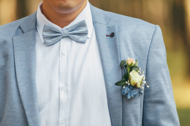 青い蝶ネクタイの青いジャケットに新郎。ジャケットの上にバラのboutonniere - 写真・画像