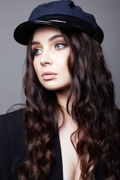 Μοντέρνο όμορφο κορίτσι με καπέλο. Κομψό όμορφη νεαρή γυναίκα με υγιή σγουρά μαλλιά - Φωτογραφία, εικόνα