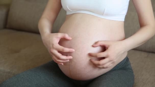 Primer plano de la mujer embarazada rascarse el estómago en el sofá
. - Metraje, vídeo