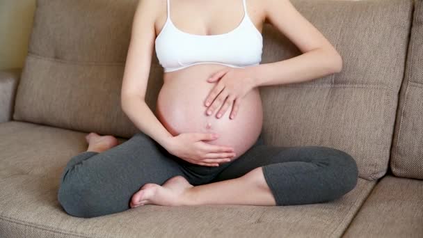 Primer plano de la mujer embarazada acariciando su estómago en el sofá
 - Metraje, vídeo