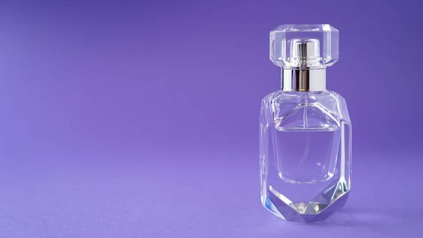 Izolált, átlátszó parfümpalack lila háttérrel. Ajándék koncepció. Az illatspray gúnyolódik. Tavaszi illat - Fotó, kép
