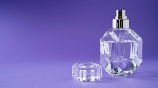 Perfumy w szklanej butelce na fioletowym tle. Diamentowy kształt butelki. Przezroczysta butelka. Kryształ. Izolacja - Zdjęcie, obraz