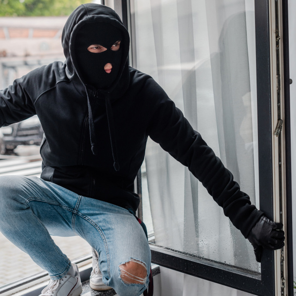 Robber en gant de cuir et cagoule debout près de la fenêtre ouverte
  - Photo, image
