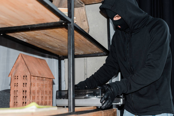 Selektywne skupienie złodzieja w kominiarce biorąc gramofon podczas napadu  - Zdjęcie, obraz
