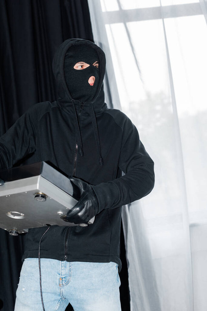 Robber in balaclava and leather glove holding record player during burglary - Photo, Image