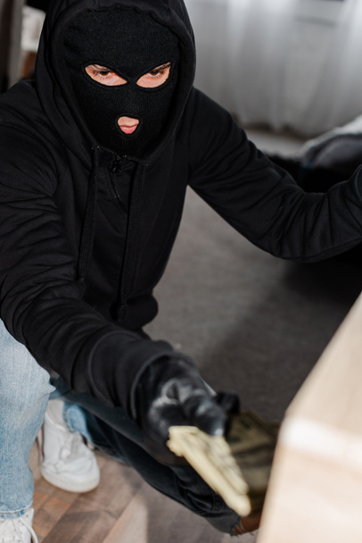 Focus selettivo del ladro in maschera che prende banconote in dollari dalla tabella durante la rapina
  - Foto, immagini