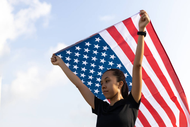 青い空を背景にアメリカ国旗を掲げる若いアジア人女性 - 写真・画像