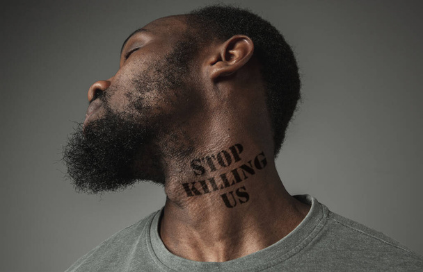 Close up portret czarnego człowieka zmęczony dyskryminacją rasową ma wytatuowany slogan na szyi - Zdjęcie, obraz