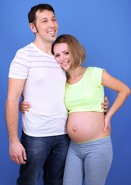 Young pregnant woman with her husband on blue background - Foto, imagen