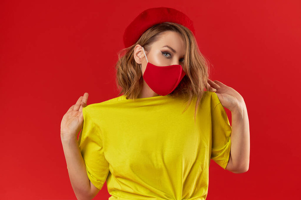 Woman in trendy fashion outfit during quarantine of coronavirus outbreak. Model dressed protective stylish handmade face mask on red studio background - Foto, imagen