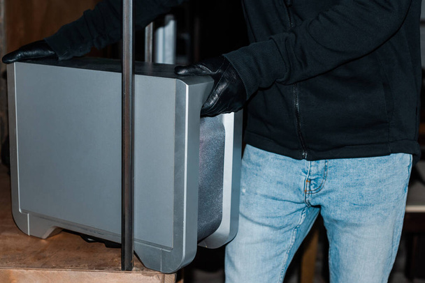 Cropped view of robber taking wireless speaker from cupboard during stealing - Photo, Image