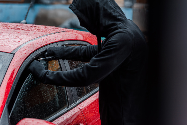 Selective focus of robber opening glass of car door with screwdriver on urban street  - Фото, зображення