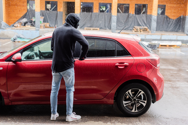 Vista trasera del ladrón mirando hacia otro lado mientras abre la puerta del coche con destornillador en la calle urbana
  - Foto, imagen