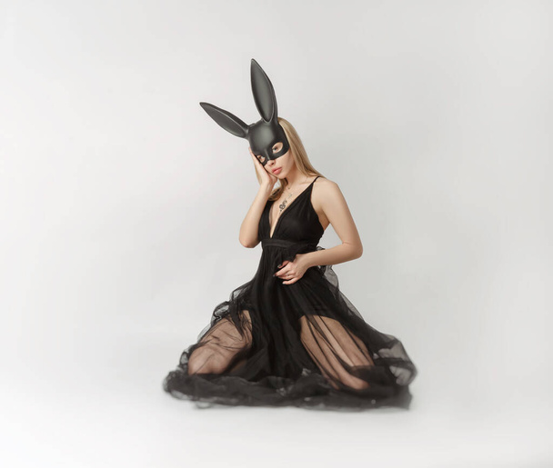 Hermosa rubia con una máscara de conejo en un vestido de noche sexy sobre un fondo blanco
 - Foto, Imagen