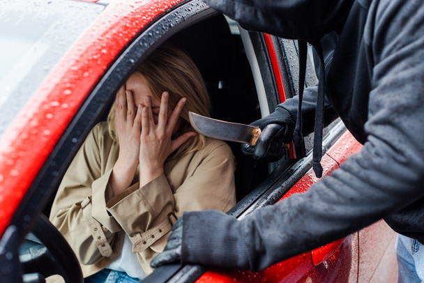 Enfoque selectivo del ladrón que sostiene el cuchillo cerca de la mujer asustada en el coche
  - Foto, Imagen