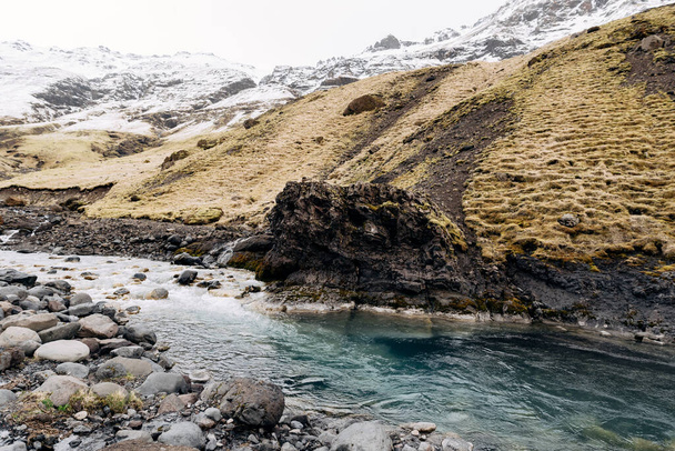 Dağ nehri dağın eteğinde karla kaplı bir tepesi var. Mayıs ayında İzlanda 'da dağlarda sarı kuru otlar. - Fotoğraf, Görsel