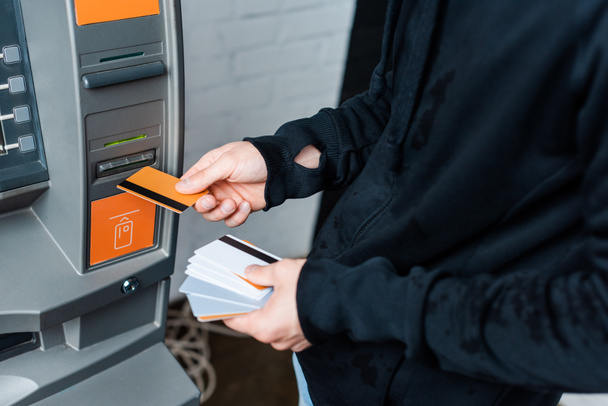 Обрізаний вигляд злодія, що тримає кредитні картки біля автоматизованого тендерного апарату
 - Фото, зображення