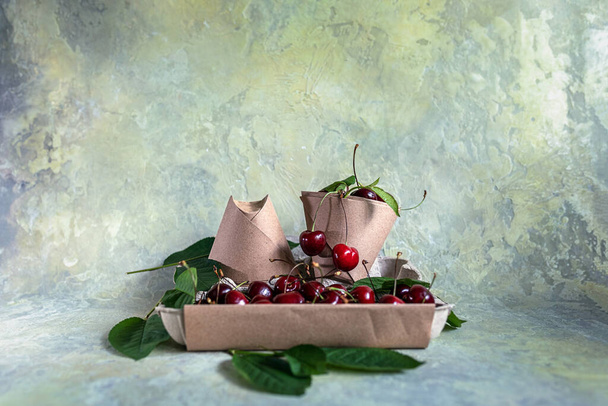 Paper cups or origami bags, containers with cherries. Eco-friendly food packaging, on an abstract beautiful background with a copy space. The preservation of nature and the concept of recycling. selective focus. - Foto, afbeelding