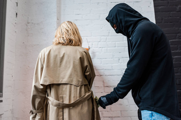 Грабитель в маске берет деньги из кармана женского пальто
  - Фото, изображение