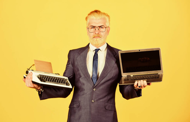mature man dyed beard hair. computer or typewriter. new and old technology. modern digital business. vintage typewriter. businessman use retro typewriter and modern laptop - Fotó, kép