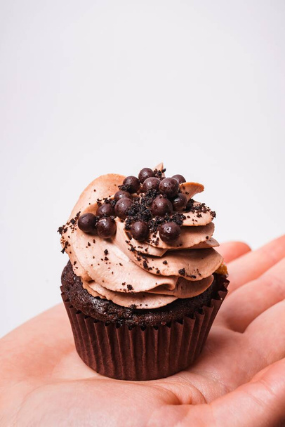 A vertical shot of a person holding a chocolate cupcake under the lights on a grey background - Fotografie, Obrázek