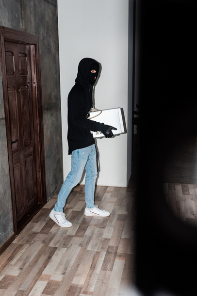 Вид збоку на грабіжника, який тримає мікрохвильову піч під час ходьби біля дверей будинку
  - Фото, зображення