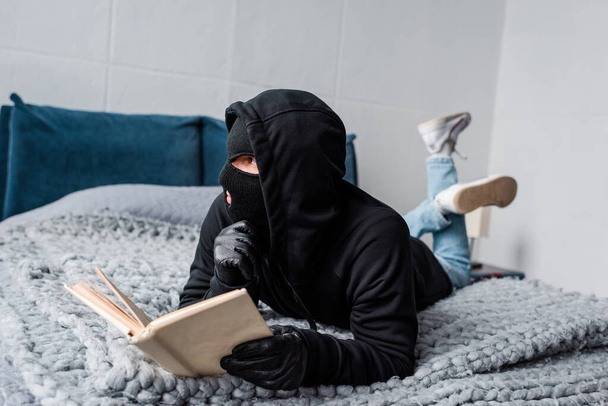 Szelektív fókusz tolvaj maszk és bőrkesztyű olvasókönyv az ágyon  - Fotó, kép
