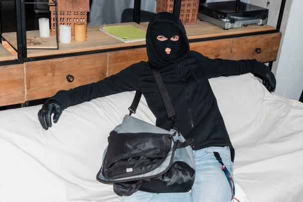 Kar maskeli bir soyguncu dizüstü bilgisayarın yanında otururken kameraya bakıyor.  - Fotoğraf, Görsel