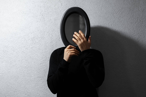 Драматический портрет юноши с черным овальным зеркалом на лице. Текстурированный абстрактный фон серой стены
. - Фото, изображение
