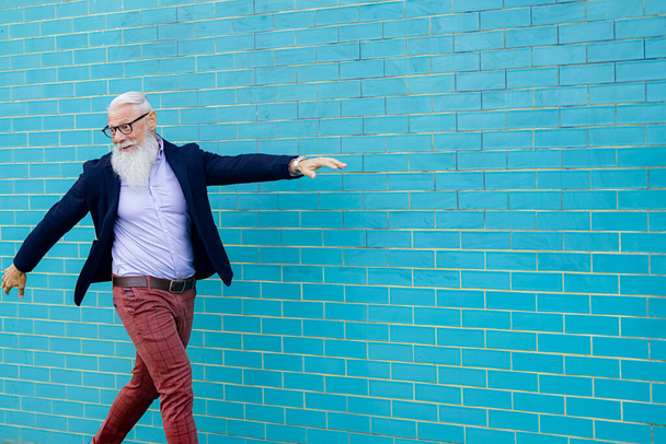 Onnellinen mies juhlimassa uutta elämää. Energinen onnellinen kypsä mies rento vaatteet kävely kaupungissa, seinä eristetty vaaleansininen tausta - Iloinen vanhusten elämäntapa käsite - Kuva - Valokuva, kuva