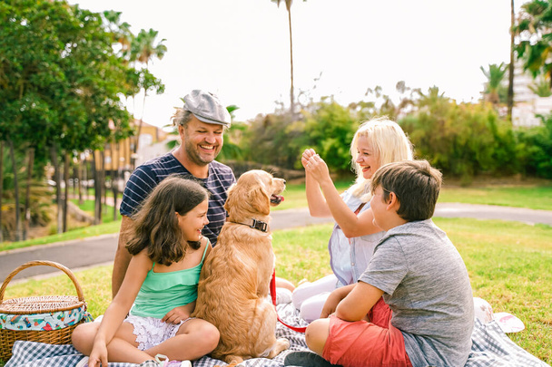 Glückliche Familie mit ihrem Hund an einem schönen Sommertag. Die Familie spielt mit Hund. Glückliche Familie beim Picknick im Park. Reise, Urlaub und Liebeskonzept - Image - Foto, Bild