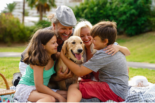 Concepto de familia feliz: madre, padre e hijos pequeños haciendo picnic en el parque de verano. El perro es muy feliz en esta familia. Enfoque al perro - Imagen
 - Foto, Imagen
