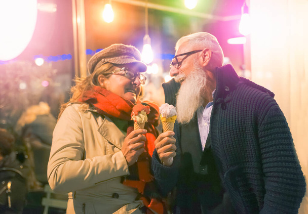 Älteres Paar beim Eis essen in verliebter Haltung - Attraktive Rentner schauen einander beim Spaß aus der Eisdiele an - Konzept von Romantik und Liebesmoment - Fokus auf Eis und Hände - Foto, Bild