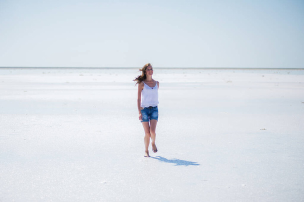 Gyönyörű fiatal lány fut és mosolyog egy száraz sós tavon nyáron délben - Fotó, kép