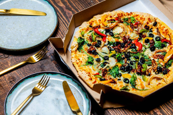 śródziemnomorska pizza z oliwkami i serem w tekturze i na talerzach na stole - Zdjęcie, obraz