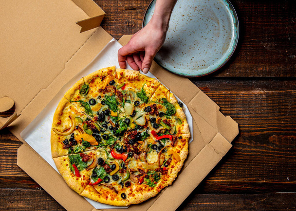 mão mulher leva uma pizza mediterrânea com azeitonas e queijo de papelão em um prato
  - Foto, Imagem