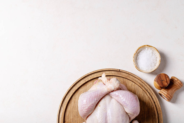 Raw whole chicken served with salt, pepper, paprika, oregano and olive oil over white texture background. Top view, flat lay. Copy space - 写真・画像