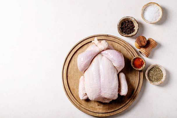 Raw whole chicken served with salt, pepper, paprika, oregano and olive oil over white texture background. Top view, flat lay. Copy space - Foto, Imagem