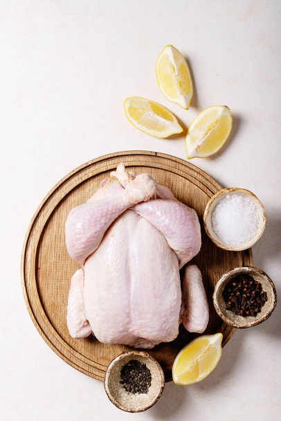 Raw whole chicken served with salt, pepper, paprika, oregano, lemon and olive oil over white texture background. Top view, flat lay. Copy space - 写真・画像