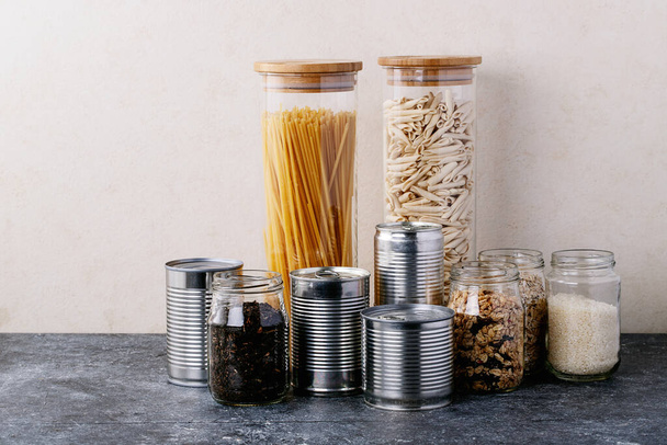 Canned food in metal cans with oats, rice, tea, and pasta in glass jars over white texture background. Copy space. Food supply concept - Fotografie, Obrázek