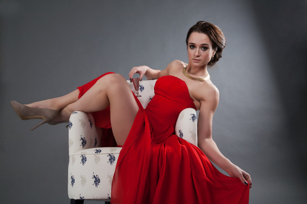 Beautiful girl in red evening dress sitting in a chair - Foto, Imagem