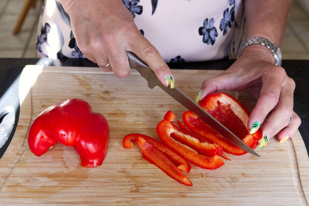 Χέρια γυναίκας που κόβει κόκκινη πιπεριά στην κουζίνα της. - Φωτογραφία, εικόνα