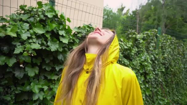 Jovem feliz em capa de chuva amarela desfrutando de chuva de verão ao ar livre. Menina sorrindo levantando braços sentindo-se bem sob chuvisco
 - Filmagem, Vídeo